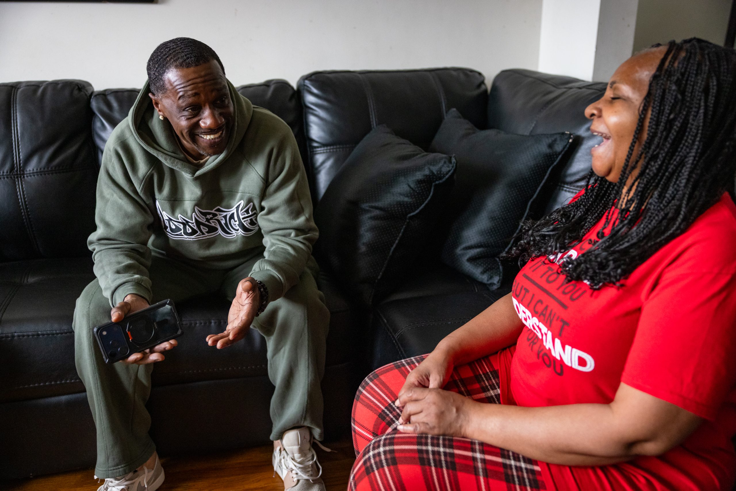 Antonio McDowell sitting on a couch with a cell phone in his hand, laughing as he talks to his mother, Florine.