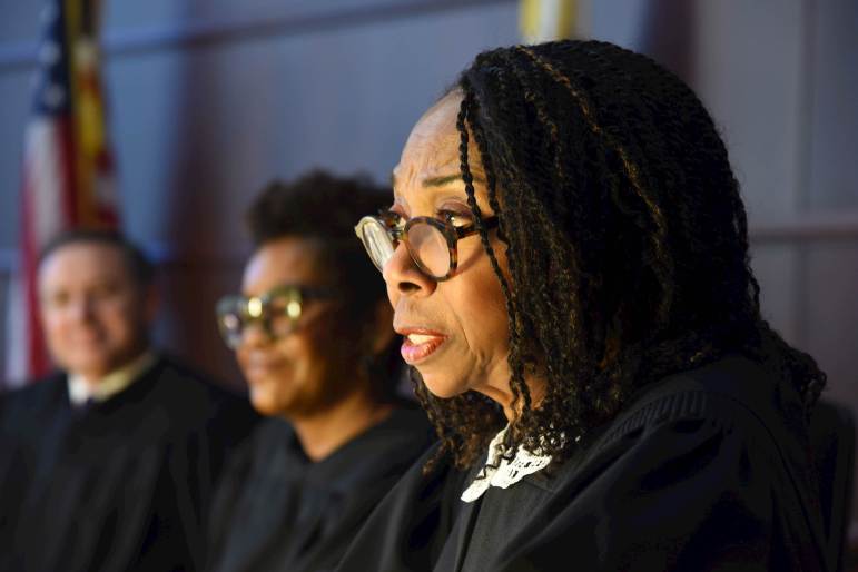 A profile of Joy Cunningham, a Black female supreme court justice, wearing a black robe and glasses with two other justices seated behind her.