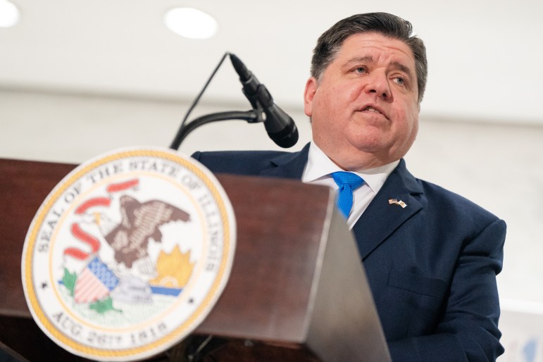 Illinois governor JB Pritzker stands behind a podium bearing the seal of the state of Illinois.