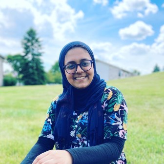 Zaina Anawarla, wearing glasses and a hijab, sits in an open field