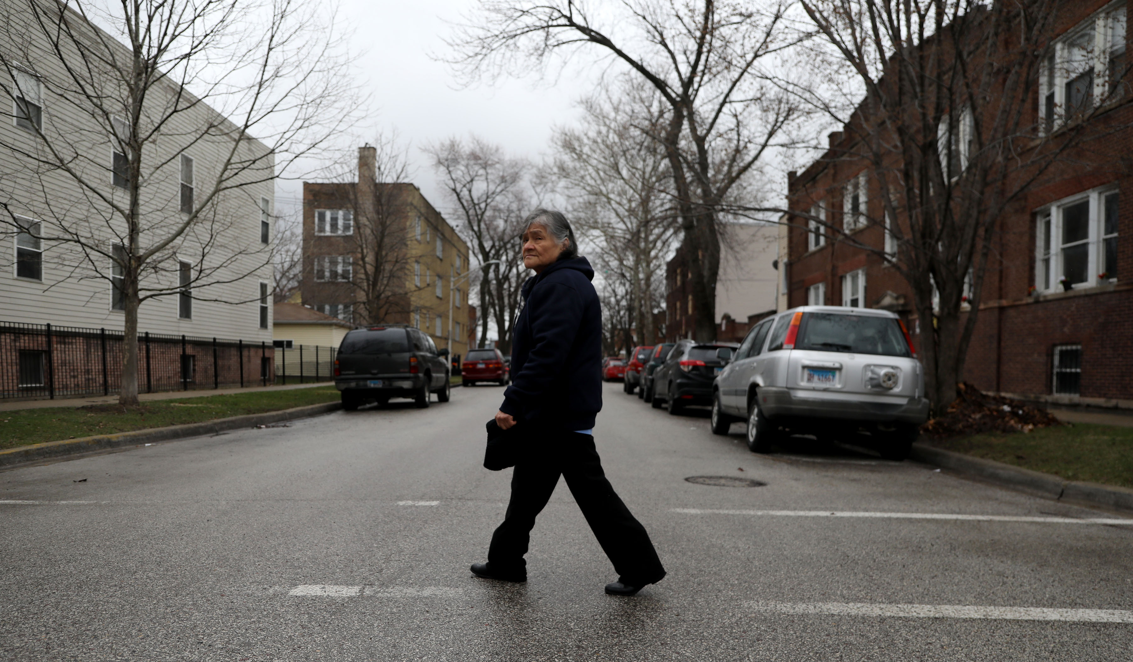A woman walks across a residential street. She's wearing a winter coat and black pants.